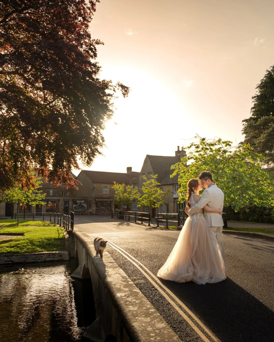 Yan & Victor embracing beside the river beneath a great copper beech at golden hour, Cotswolds village — Cotswolds pre-wedding by Kenn Photographic Arts
