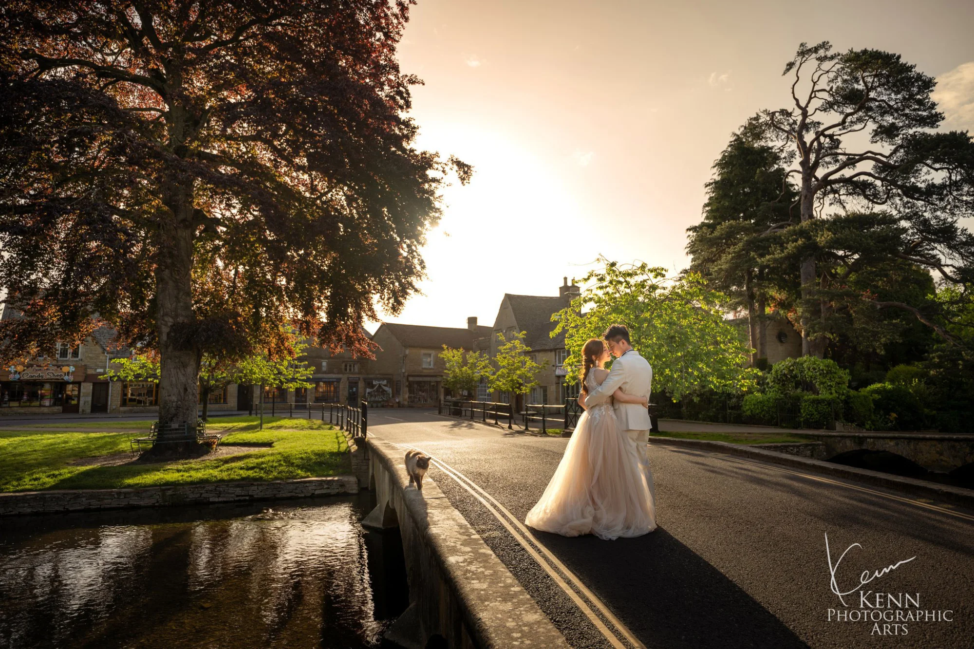 Yan & Victor embracing beside the river beneath a great copper beech at golden hour, Cotswolds village — Cotswolds pre-wedding by Kenn Photographic Arts
