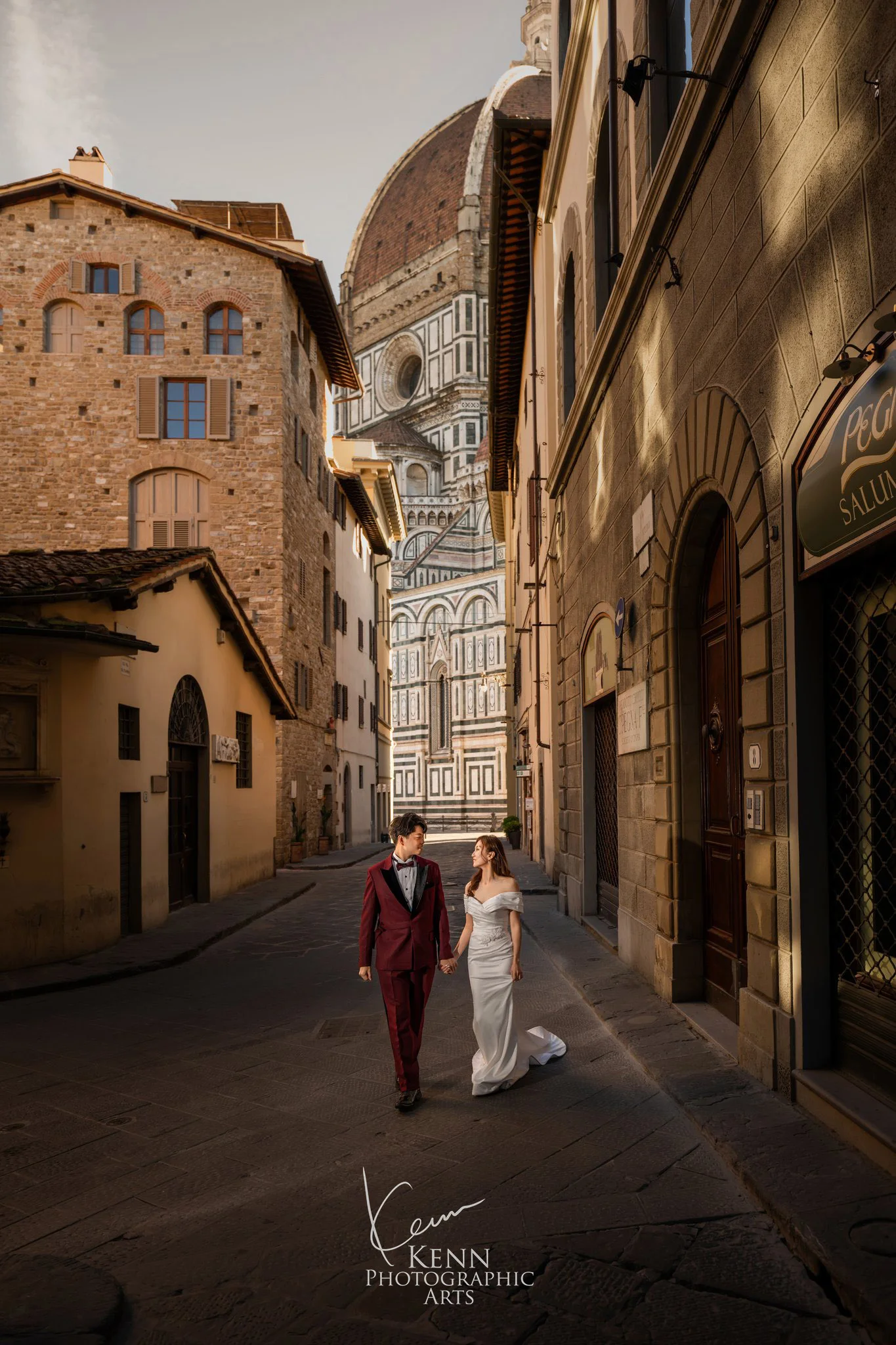 Wincy & Leo walking a narrow Florentine lane with Brunelleschi’s dome behind — Florence & Tuscany pre-wedding by Kenn Photographic Arts