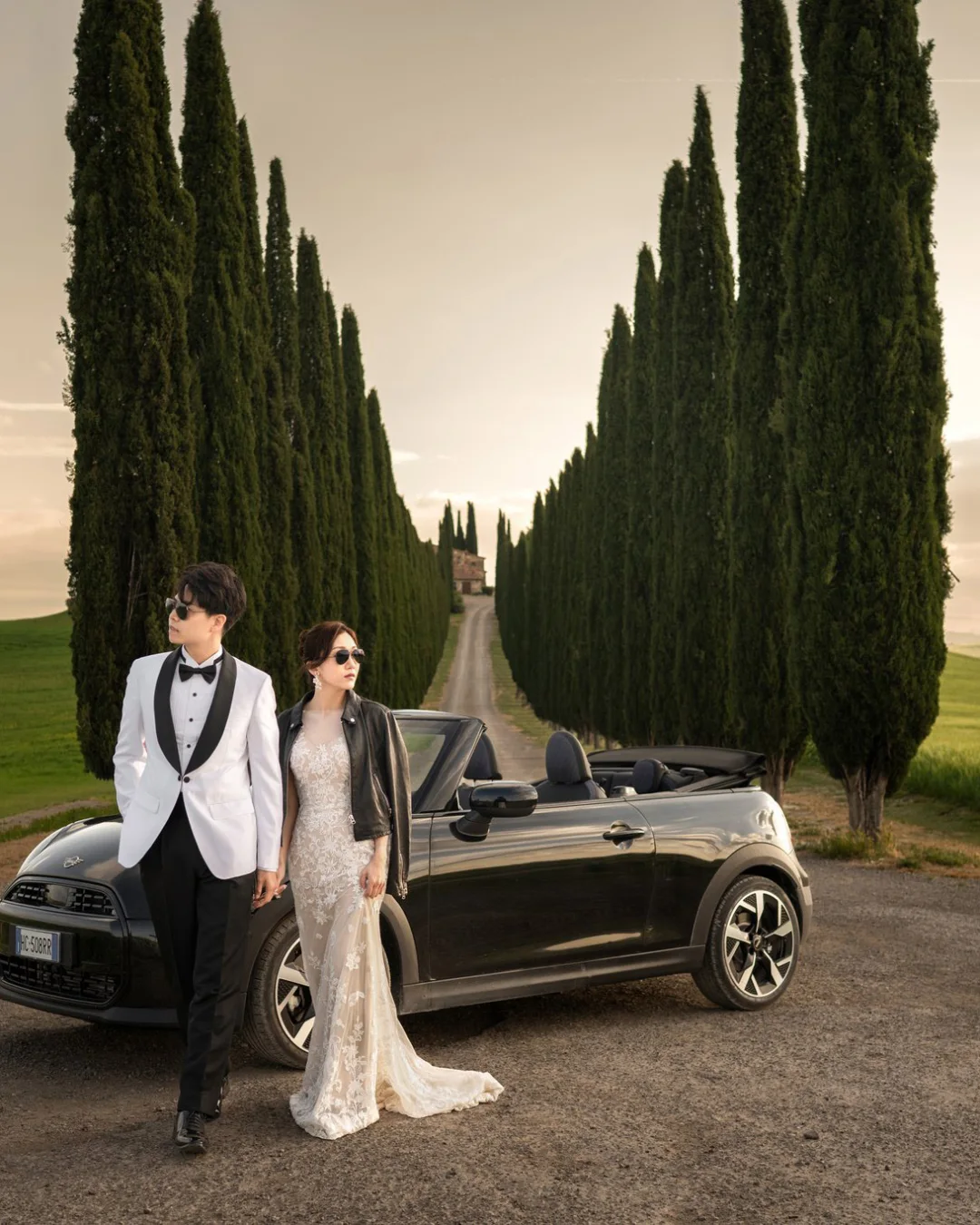 Wincy & Leo standing by a black convertible between rows of cypress trees, Val d’Orcia — Florence & Tuscany pre-wedding by Kenn Photographic Arts