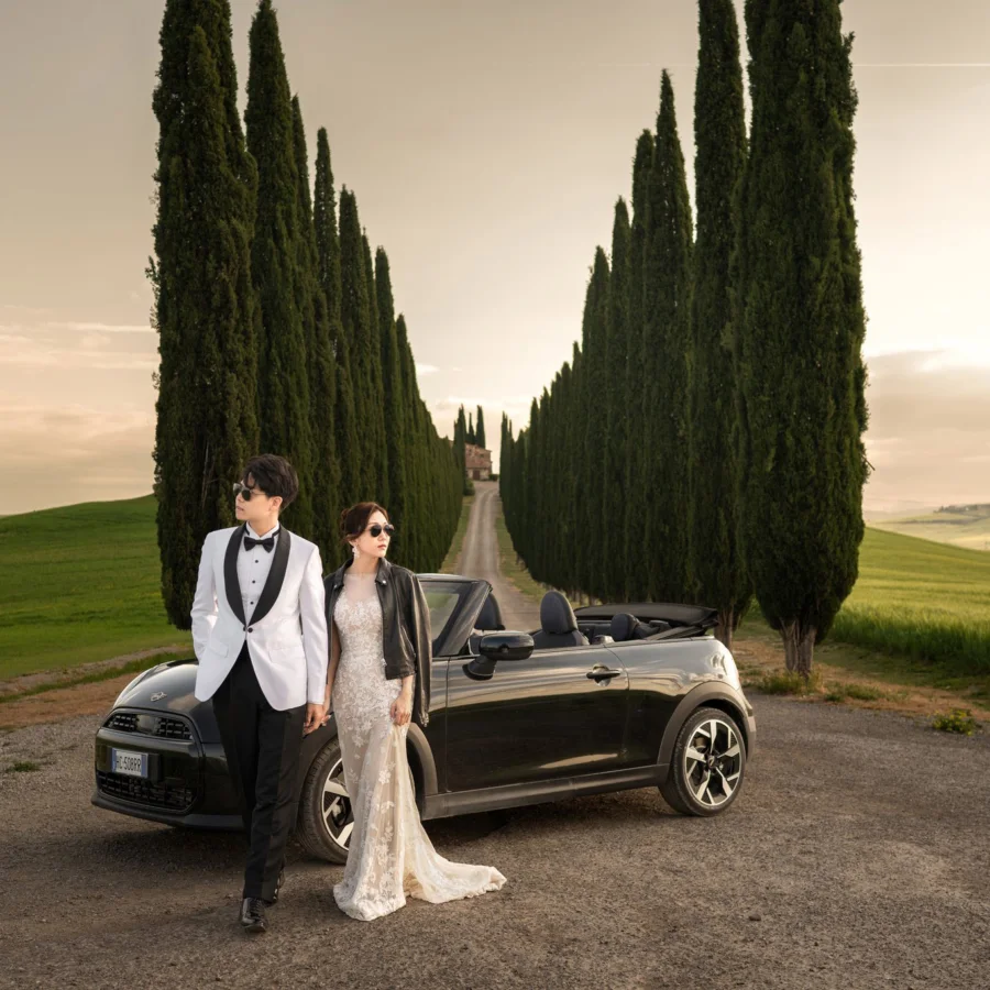 Wincy & Leo standing by a black convertible between rows of cypress trees, Val d’Orcia — Florence & Tuscany pre-wedding by Kenn Photographic Arts