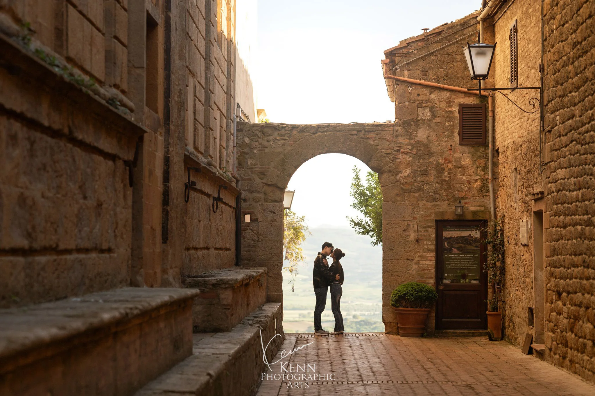 Wincy & Leo beneath a stone archway in the hill town of Pienza — Florence & Tuscany pre-wedding by Kenn Photographic Arts
