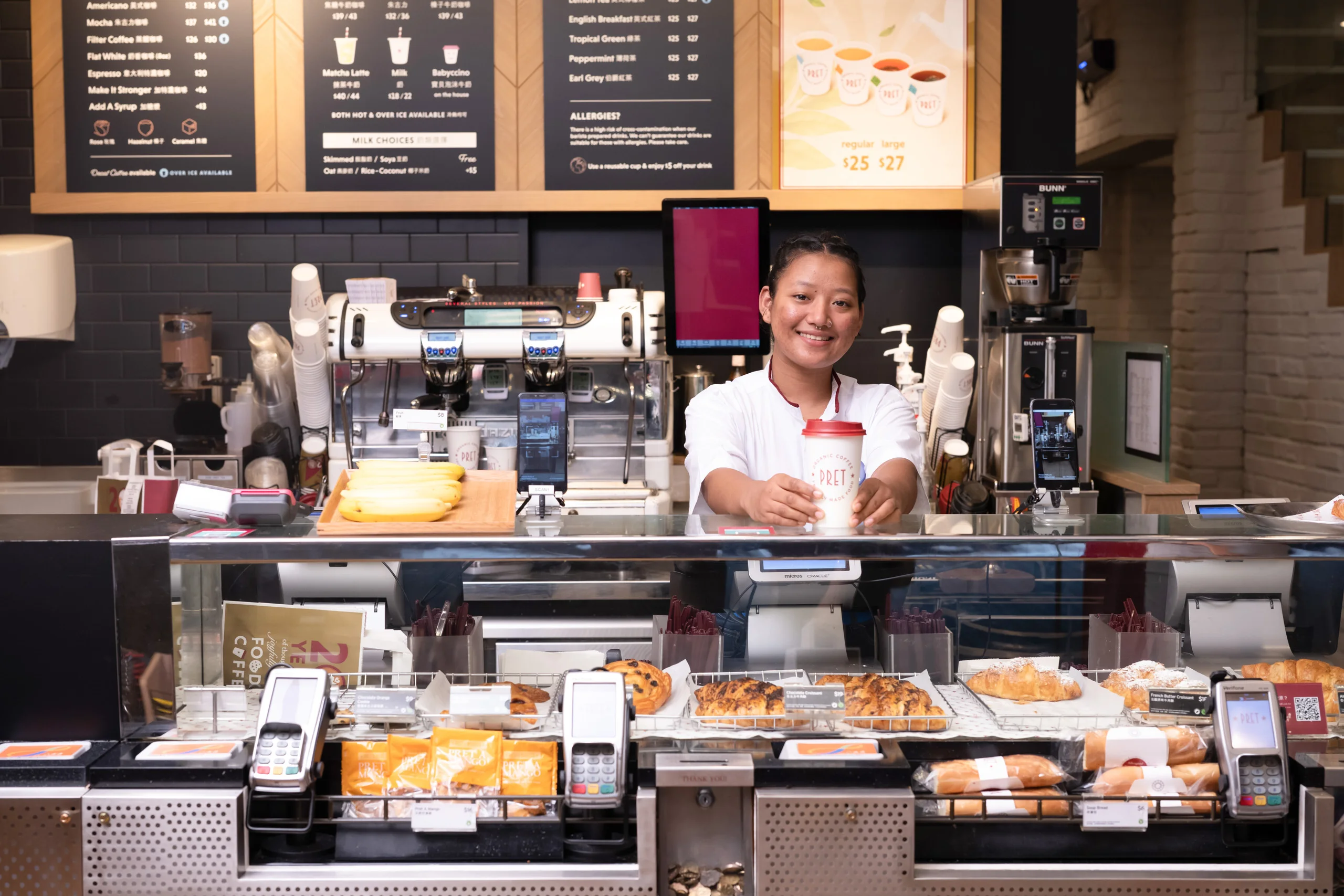 Smiling barista at a café counter with fresh pastries — food and beverage photography by Kenn Photographic Arts