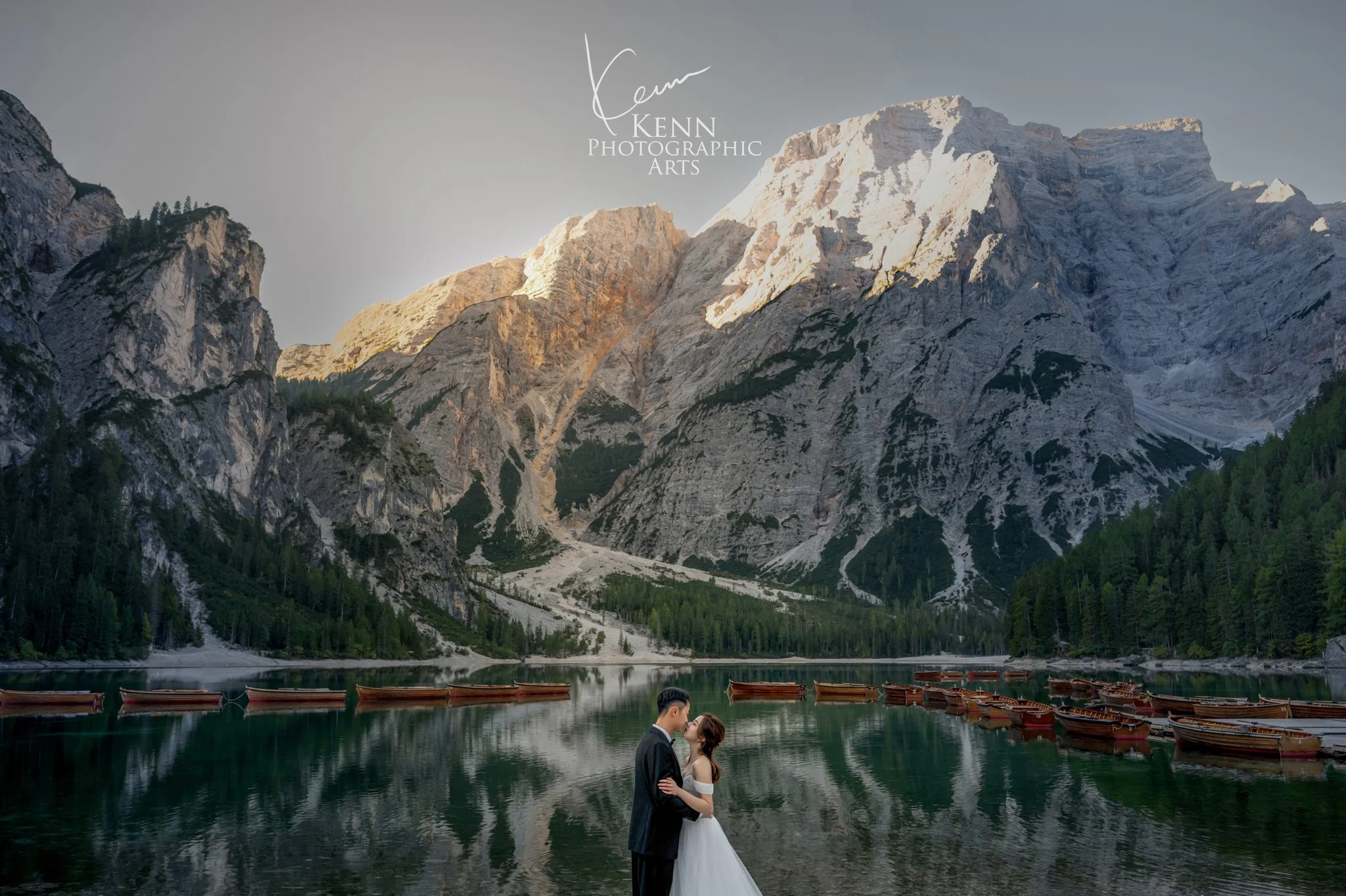 Wide view of Lago di Braies and the Seekofel peak, the couple standing by the wooden rowboats — Dolomites pre-wedding by Kenn Photographic Arts