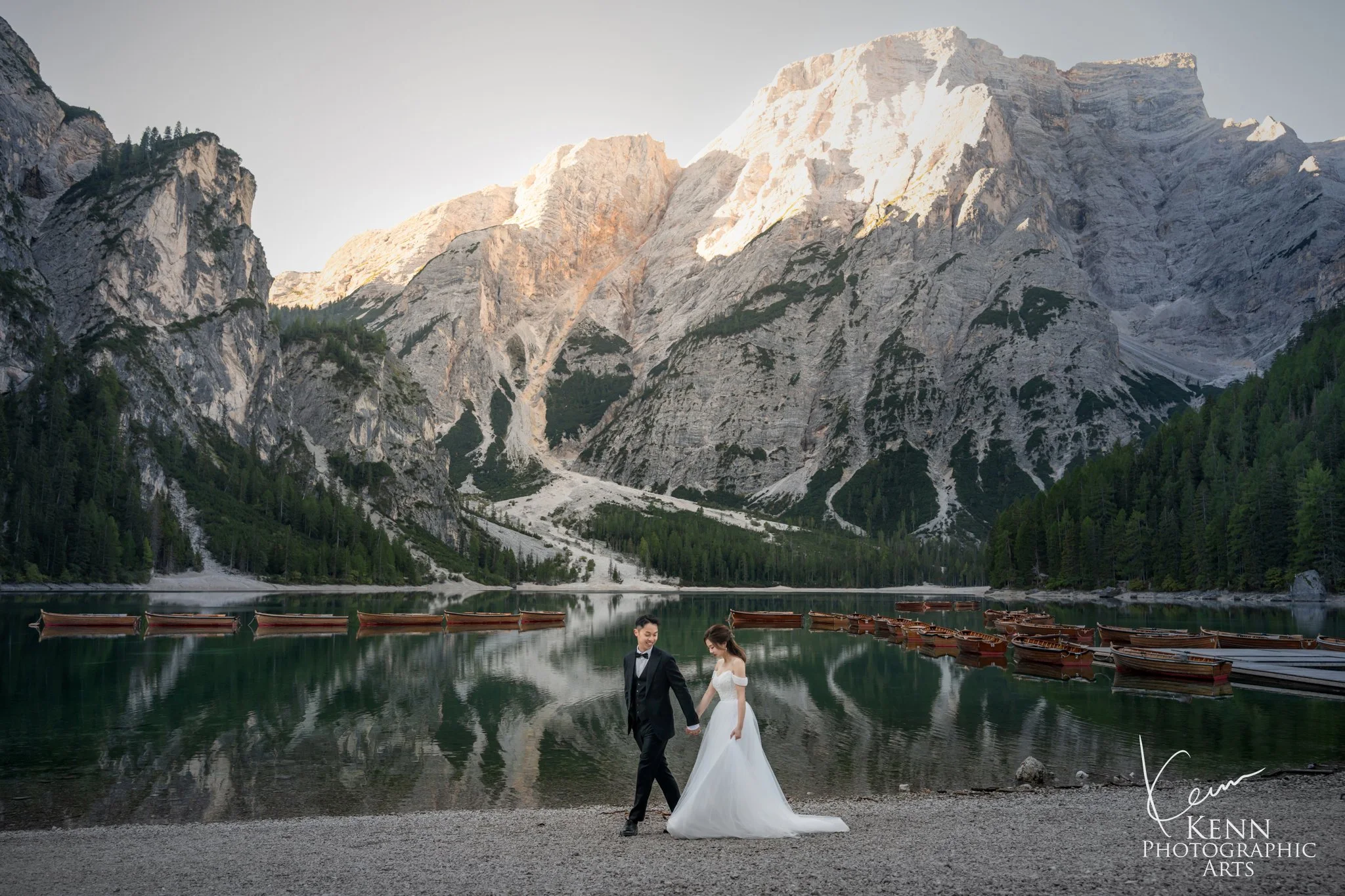 Mable & Hon walking hand in hand along the lakeshore below the Dolomite peaks — Dolomites pre-wedding by Kenn Photographic Arts