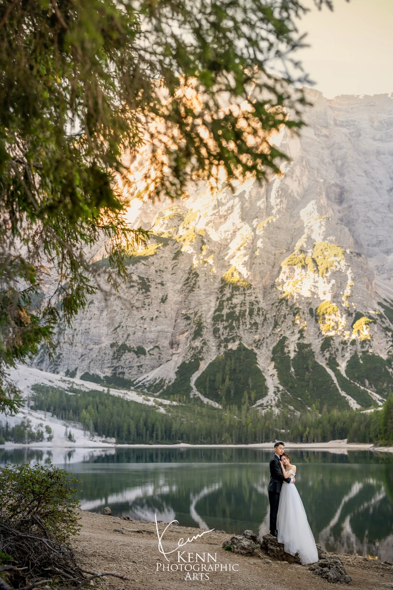 Mable & Hon beneath the pines with the peaks reflected in Lago di Braies — Dolomites pre-wedding by Kenn Photographic Arts