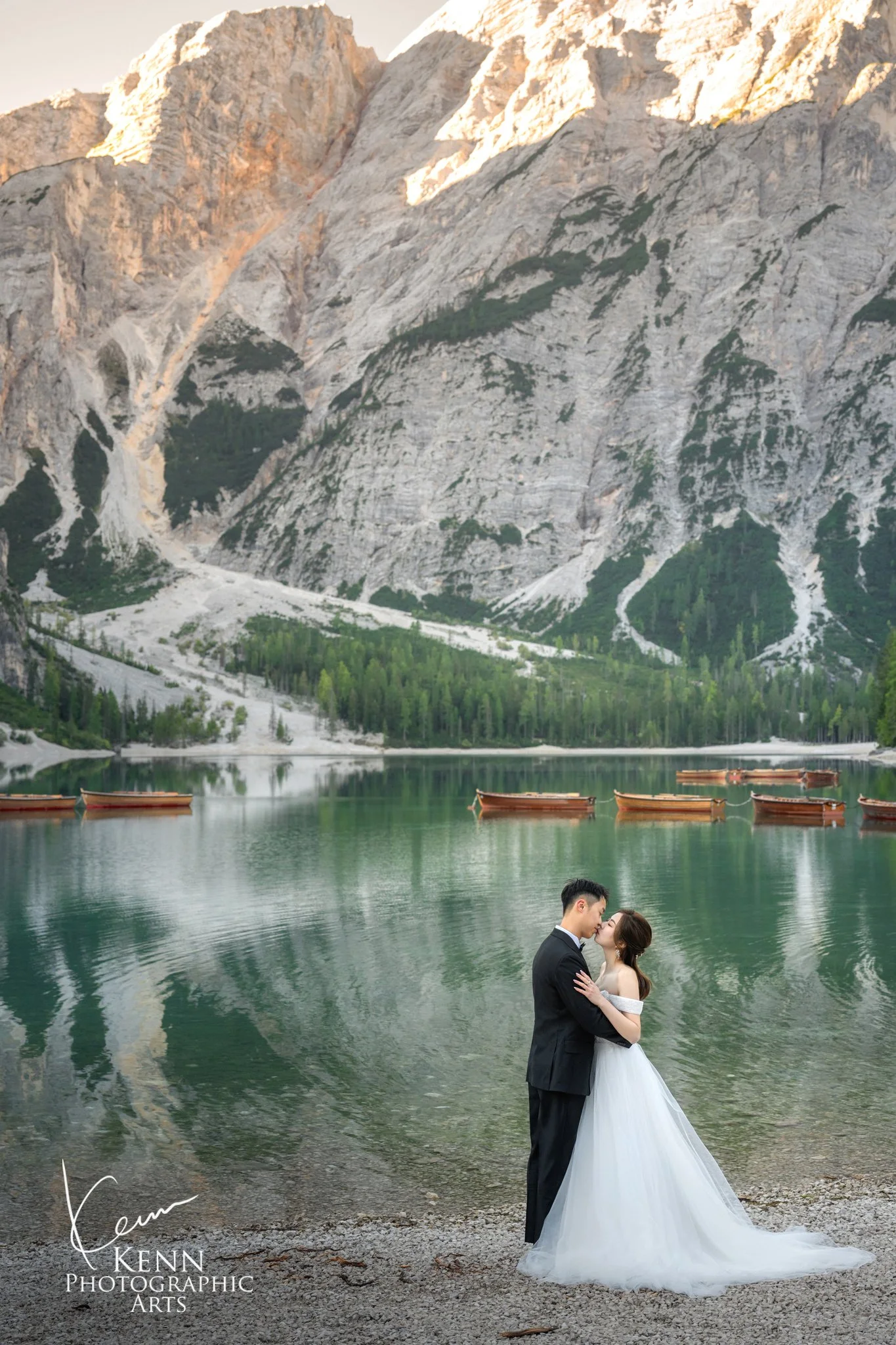 Mable & Hon embracing on the shore with the Dolomite peaks behind — Dolomites pre-wedding by Kenn Photographic Arts