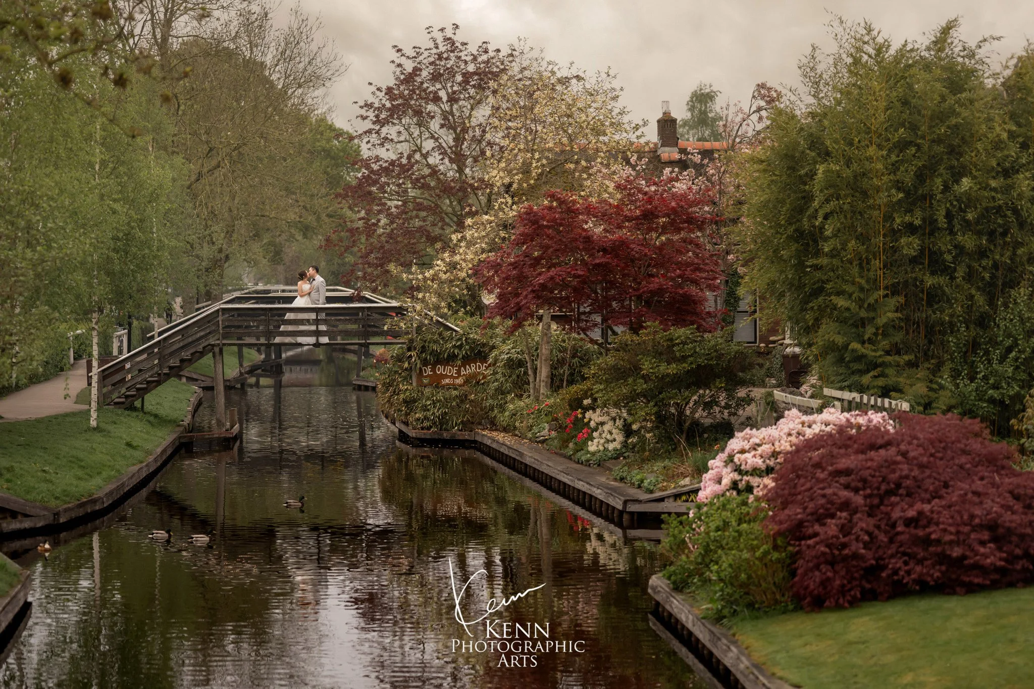 Wide view of a Giethoorn canal, footbridge and red maples with the couple on the bridge — Netherlands pre-wedding by Kenn Photographic Arts