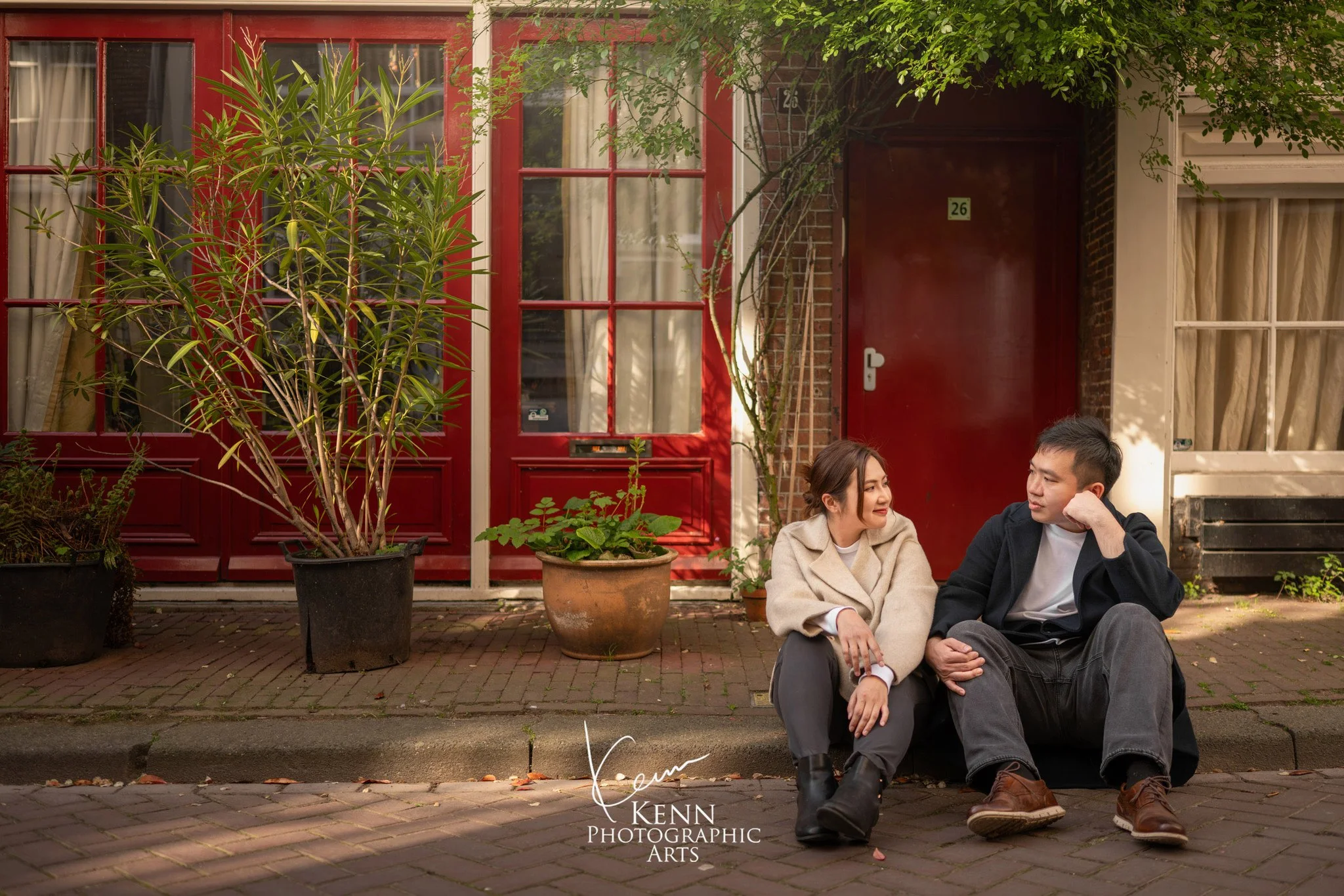 Michelle & Vincent sitting outside a red-framed doorway in Amsterdam — Netherlands pre-wedding by Kenn Photographic Arts